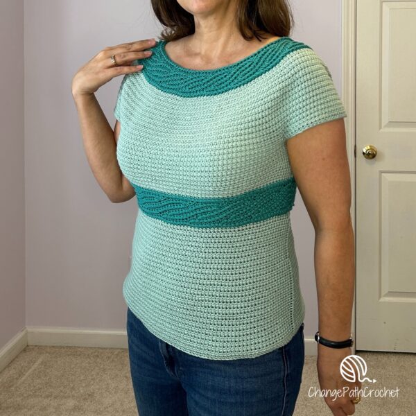 The torso of a woman wearing a short-sleeve crochet top, with swirly bands at the collar and waist.